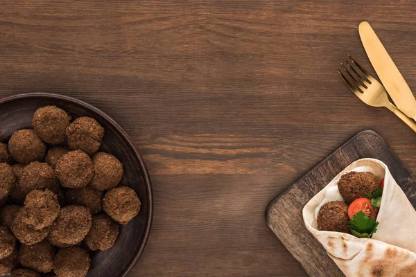 Vue du dessus de falafel aux légumes et sauce en pita près des boules et couverts sur table en bois — Photo de stock
