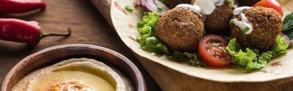 Vista de perto de falafel com verduras e molho em pita perto de hummus na mesa de madeira, tiro panorâmico — Fotografia de Stock