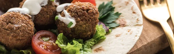 Close up view of falafel with vegetables and sauce on pita on wooden table near cutlery, panoramic shot — Stock Photo