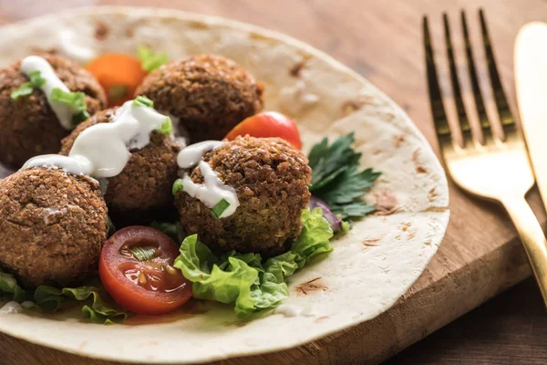 Close up view of falafel with vegetables and sauce on pita on wooden table near cutlery — Stock Photo