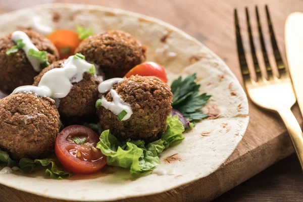 Vista ravvicinata di falafel con verdure e salsa su pita su tavolo di legno vicino a posate — Foto stock