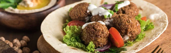 Vista de perto de falafel em pita com verduras e molho perto de hummus na mesa de madeira, tiro panorâmico — Fotografia de Stock