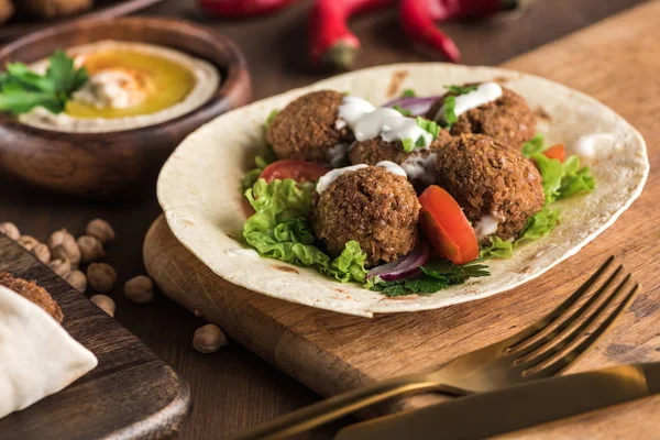 Close up view of falafel on pita with vegetables and sauce near hummus on wooden table — Stock Photo