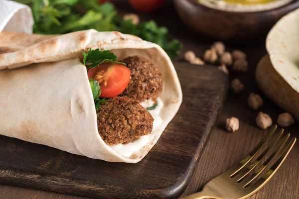 Primer plano vista de falafel con verduras y salsa envuelta en pita sobre mesa de madera - foto de stock