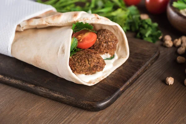 Vista de perto de falafel com legumes e molho envolto em pita na mesa de madeira — Fotografia de Stock