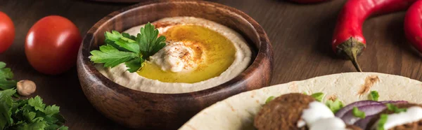 Vista de perto de falafel com verduras e molho em pita perto de hummus fresco na mesa de madeira, tiro panorâmico — Fotografia de Stock