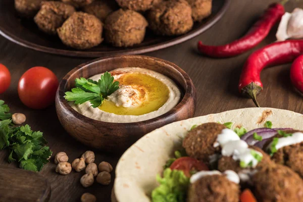 Close up view of falafel with vegetables and sauce on pita near fresh hummus on wooden table — Stock Photo