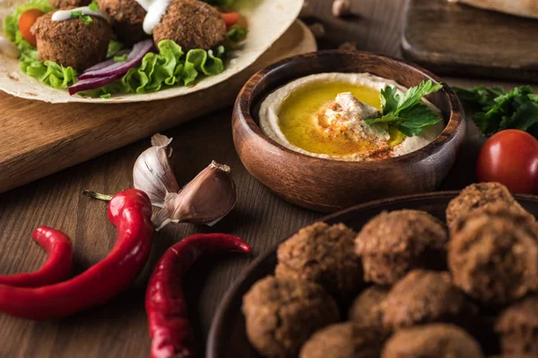 Vista ravvicinata di falafel vicino a hummus fresco, spezie e verdure sul tavolo di legno — Foto stock