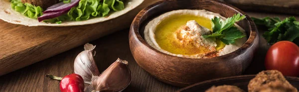 Vista de perto de hummus fresco, temperos e legumes na mesa de madeira, tiro panorâmico — Fotografia de Stock