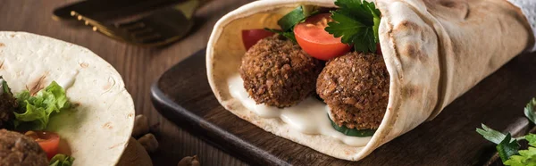 Primer plano vista de falafel con verduras y salsa en pita sobre mesa de madera, plano panorámico - foto de stock