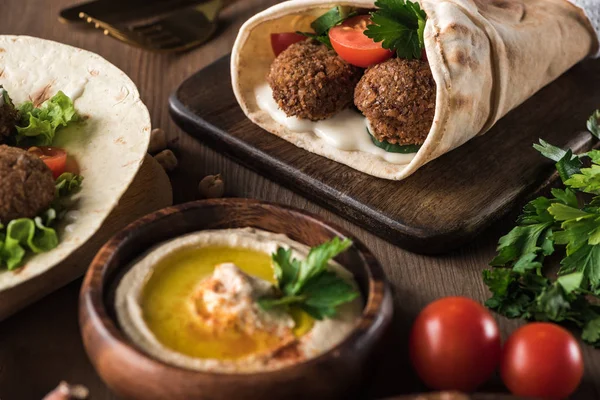 Foco seletivo de falafel com verduras e molho em pita perto de hummus na mesa de madeira — Fotografia de Stock