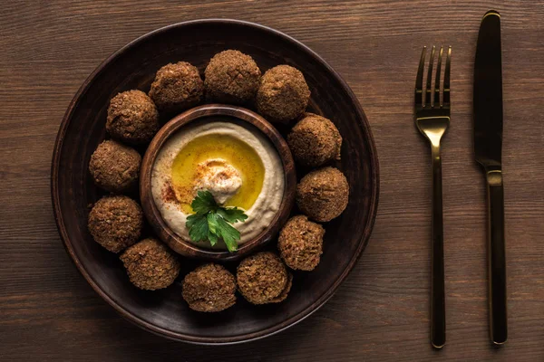 Top view of falafel balls with hummus on plate near cutlery on wooden table — Stock Photo