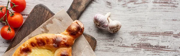 Top view of adjarian khachapuri with tomatoes and garlic on table, panoramic shot — Stock Photo