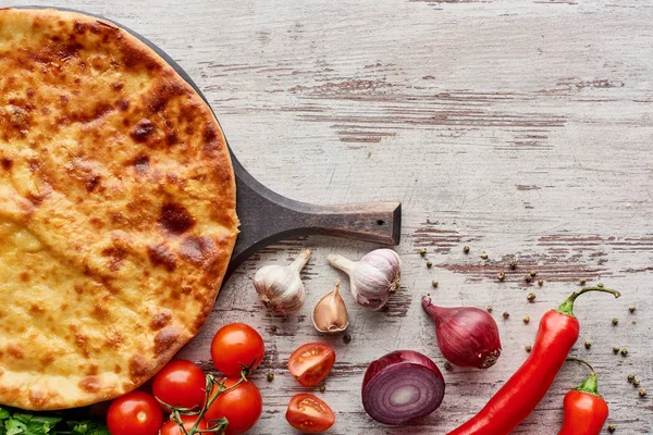 Top view of Imereti khachapuri on cutting board with vegetables and spices on table — Stock Photo