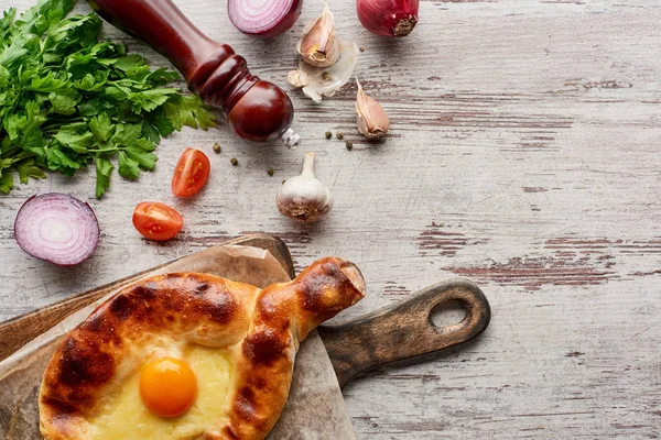 Vista superior del molino de pimienta con adjarian khachapuri y verduras en la mesa de madera — Stock Photo