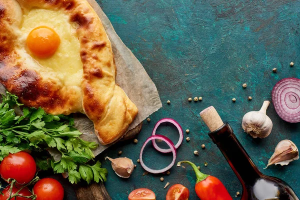 Top view of adjarian khachapuri with wine bottle and vegetables on textured green background — Stock Photo