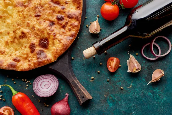 Vista superior de imereti khachapuri con botella de vino y verduras sobre fondo verde texturizado - foto de stock