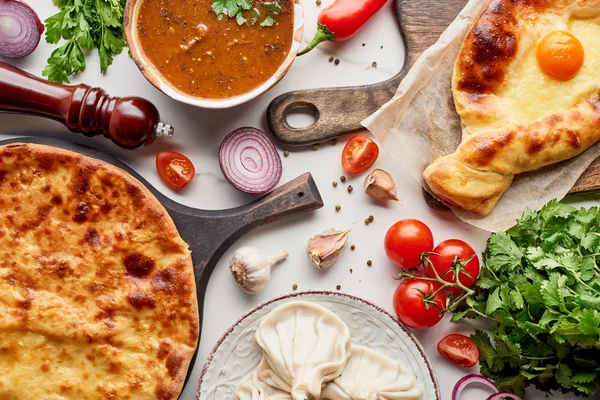 Draufsicht auf adjarianische und imereti khachapuri, Suppe kharcho und khinkali mit Gemüse auf Marmorstruktur — Stockfoto