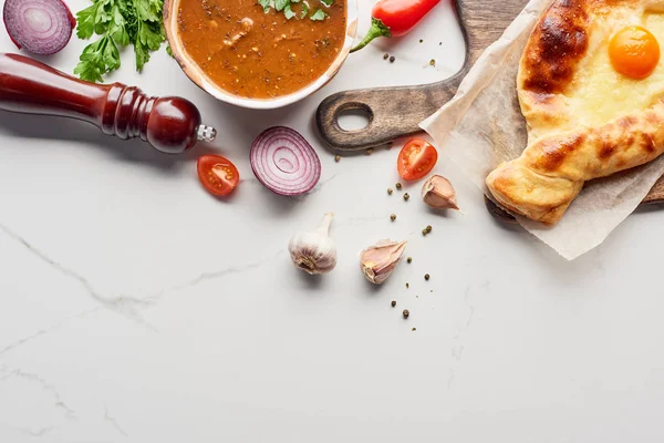 Вид зверху на аджарський хачапурі, суп харчо та овочі на мармуровій текстурі — стокове фото
