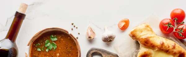 Adjarian khachapuri, soup kharcho, wine bottle and vegetables on marble texture, panoramic shot — Stock Photo