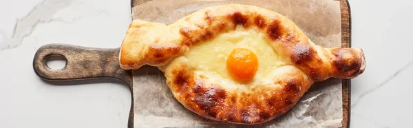 Top view of adjarian khachapuri on chopping board on marble texture, panoramic shot — Stock Photo