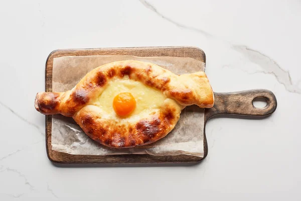 Top view of traditional adjarian khachapuri on chopping board on marble texture — Stock Photo