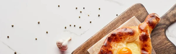 Adjarian khachapuri on cutting board with garlic and pepper on marble texture, panoramic shot — Stock Photo