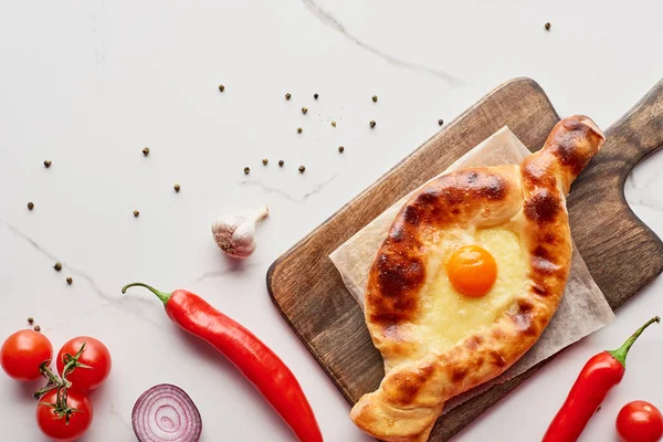 Top view of adjarian khachapuri on cutting board with vegetables on marble texture — Stock Photo