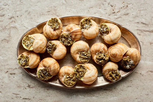 Vista superior de deliciosas escargotas cocidas en plato sobre fondo de piedra - foto de stock