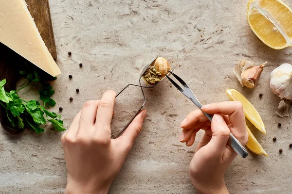 Vue partielle de femme mangeant de délicieux escargots cuits avec une pince à épiler sur fond de pierre près des ingrédients — Photo de stock