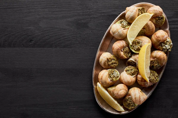 Blick von oben auf köstliche gekochte Escargots mit Zitrone auf schwarzem Holztisch — Stockfoto