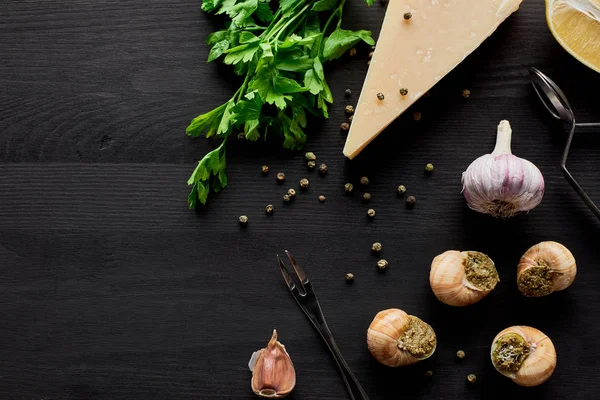 Vue de dessus de délicieux escargots cuits sur table en bois noir avec des ingrédients — Photo de stock