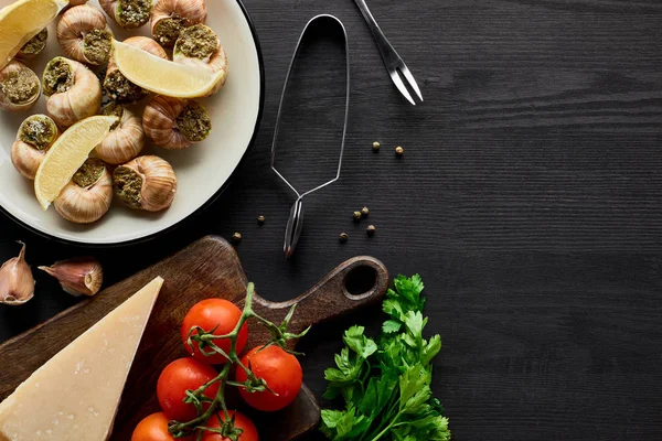 Vista superior de deliciosos escargots cozidos com fatias de limão em mesa de madeira preta com ingredientes — Fotografia de Stock