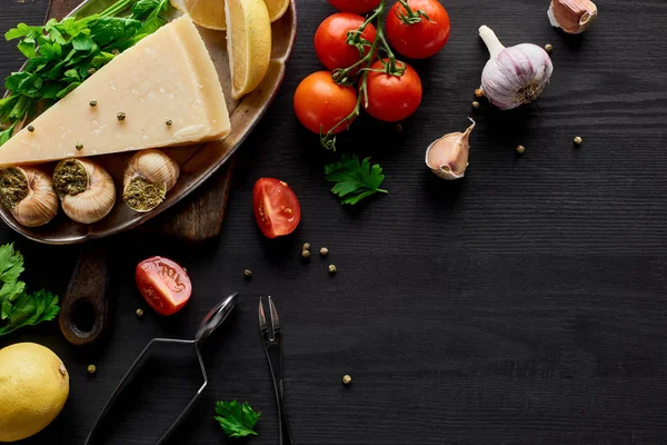 Draufsicht auf köstlich gekochte Escargots auf schwarzem Holztisch mit Zutaten — Stockfoto