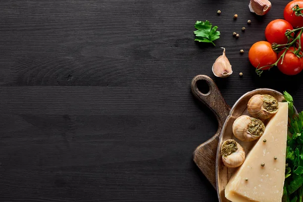 Top view of delicious cooked escargots on black wooden table with ingredients — Stock Photo