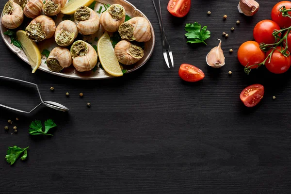 Draufsicht auf köstlich gekochte Escargots auf schwarzem Holztisch mit Zutaten — Stockfoto