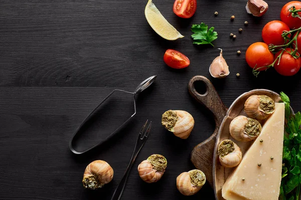 Vue de dessus de délicieux escargots cuits sur table en bois noir avec des ingrédients — Photo de stock