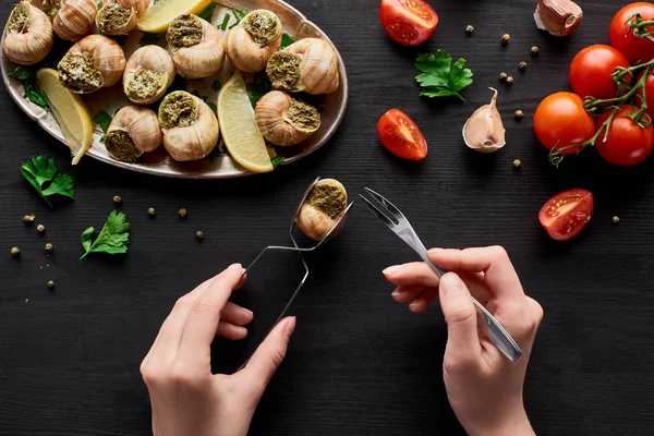 Vista recortada de la mujer comiendo deliciosas escargots con limón en la mesa de madera negro — Stock Photo
