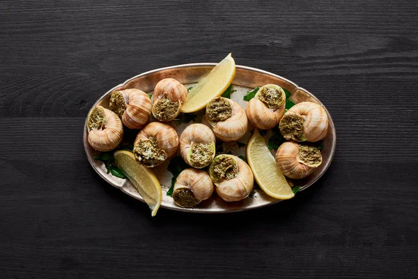 Blick von oben auf köstliche gekochte Escargots mit Zitrone auf schwarzem Holztisch — Stockfoto