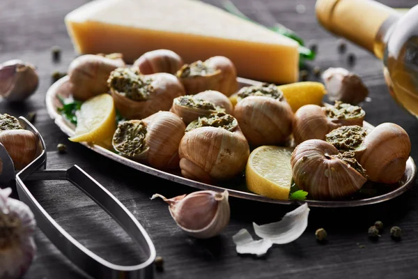 Delicious cooked escargots with lemon slices on black wooden table with spices and white wine — Stock Photo