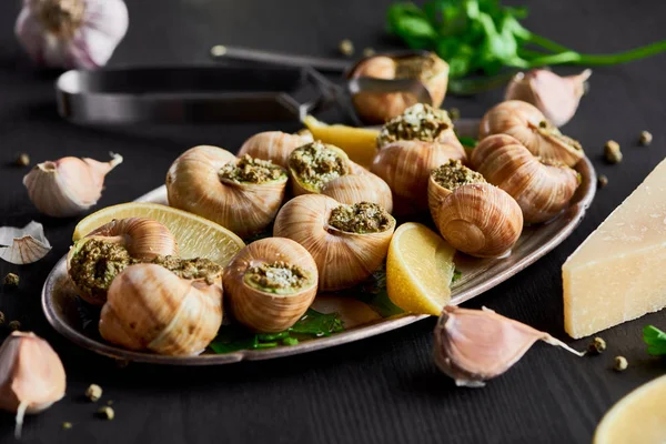 Deliciosos escargots cozidos com fatias de limão na mesa de madeira preta — Fotografia de Stock