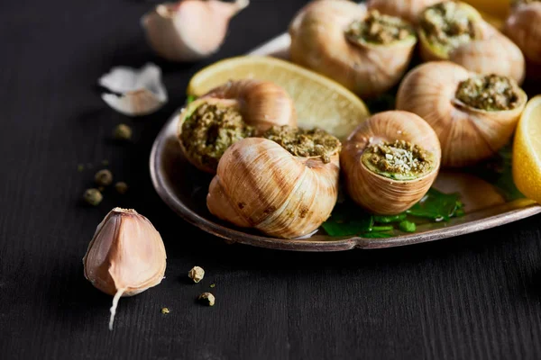 Vista de cerca de deliciosas escargots cocidas con rodajas de limón y ajo - foto de stock