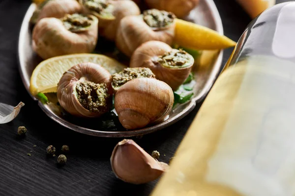 Vista de cerca de deliciosas escargots cocidas con rodajas de limón cerca del vino blanco - foto de stock