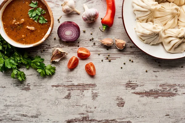 Top view of delicious khinkali and kharcho near vegetables and spices on wooden table with copy space — Stock Photo