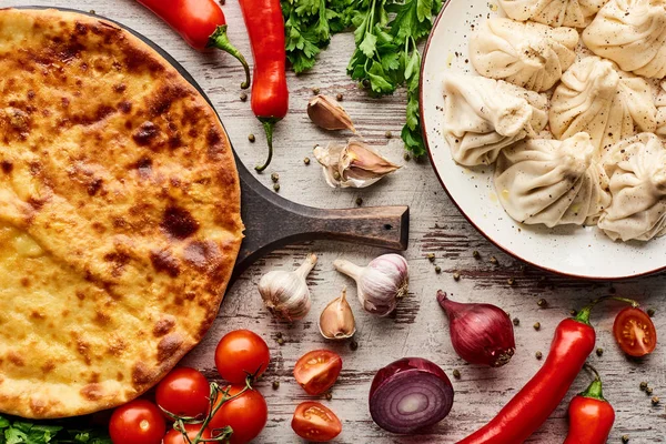 Top view of delicious Imeretian khachapuri and khinkali near vegetables and spices on wooden table — Stock Photo