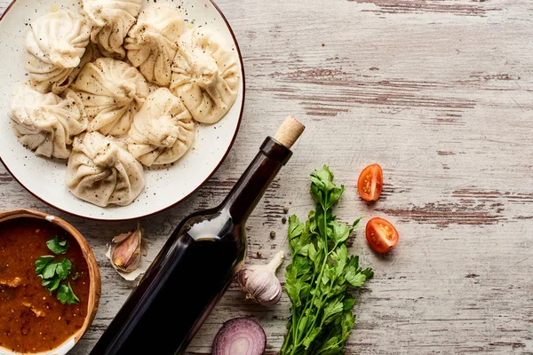 Blick von oben auf köstliches Chinkali in der Nähe einer Flasche Wein, Chartscho, Gemüse und Gewürzen auf einem Holztisch — Stockfoto