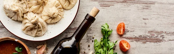 Top view of delicious khinkali near bottle of wine, kharcho, vegetables and spices on wooden table, panoramic shot — Stock Photo