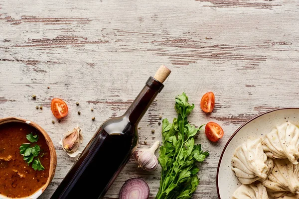 Vista dall'alto di deliziosi khinkali vicino a bottiglia di vino, kharcho, verdure e spezie sul tavolo di legno — Foto stock