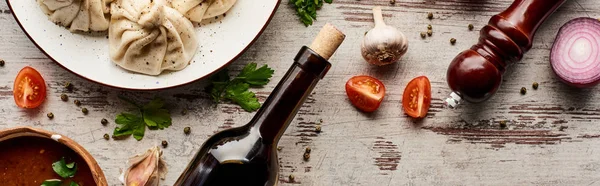 Top view of delicious khinkali near bottle of wine, kharcho, vegetables and spices on wooden table, panoramic shot — Stock Photo
