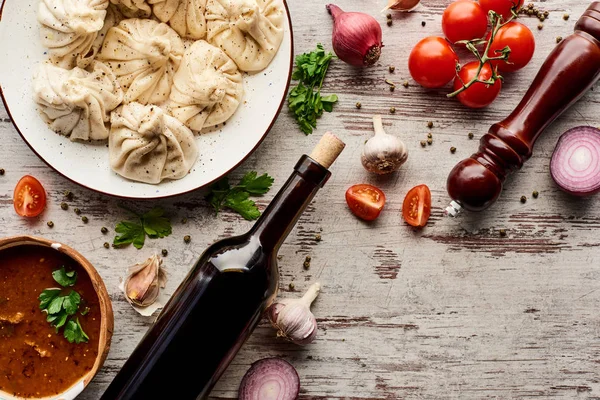 Blick von oben auf köstliches Chinkali in der Nähe einer Flasche Wein, Chartscho, Gemüse und Gewürzen auf einem Holztisch — Stockfoto